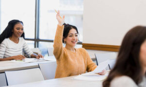 The student raises her hand to ask a question about the assignment she is working on.