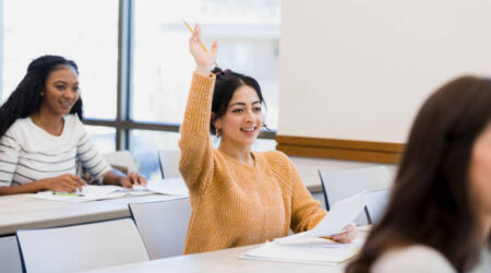 The student raises her hand to ask a question about the assignment she is working on.