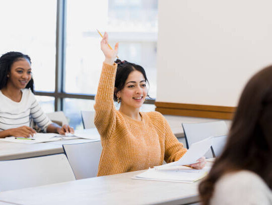 The student raises her hand to ask a question about the assignment she is working on.